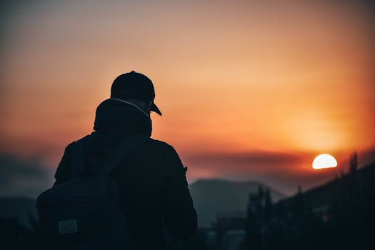 A person silhouetted during sunset in a scenic mountain landscape, capturing the essence of outdoor adventure and travel.